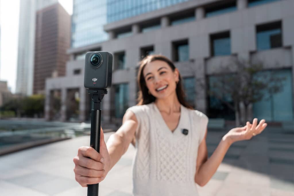 Mulher a gravar com uma câmara DJI Osmo 360 num selfie stick, em ambiente urbano.
